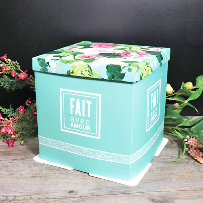 Boîte pâtissière turquoise « Fait avec amour » avec couvercle à motifs floraux, présentée dans un décor fleuri
