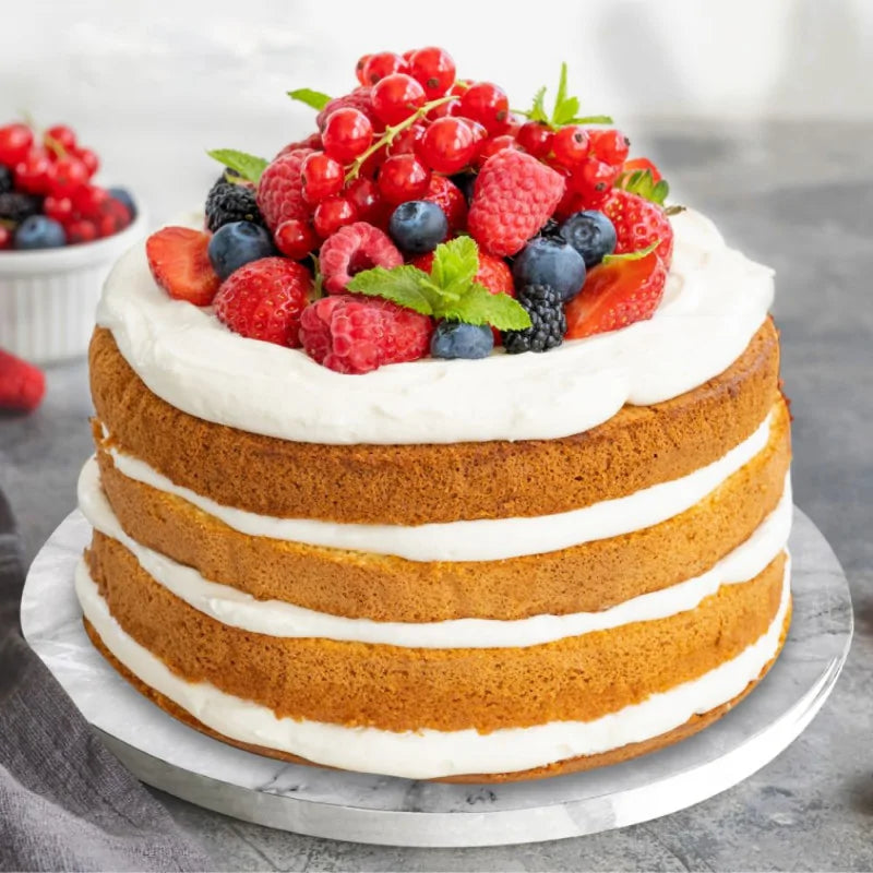 Gâteau à étages garni de crème et fruits rouges, présenté sur un plateau rond effet marbre blanc