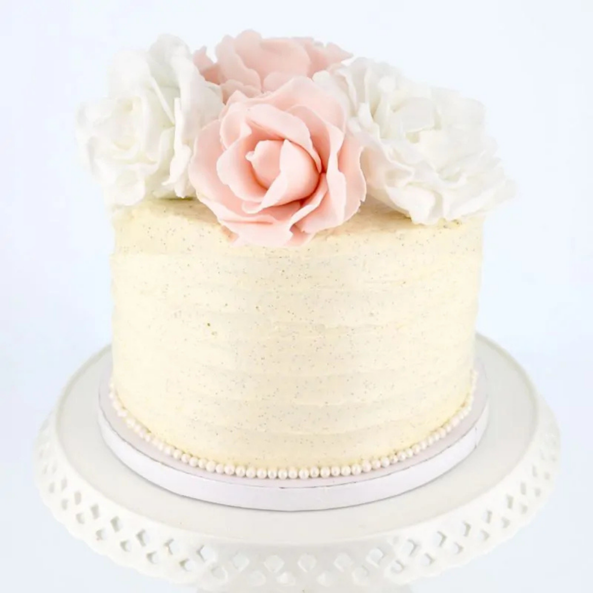 Gâteau décoré de fleurs roses et blanches présenté sur une plateau ronde blanche