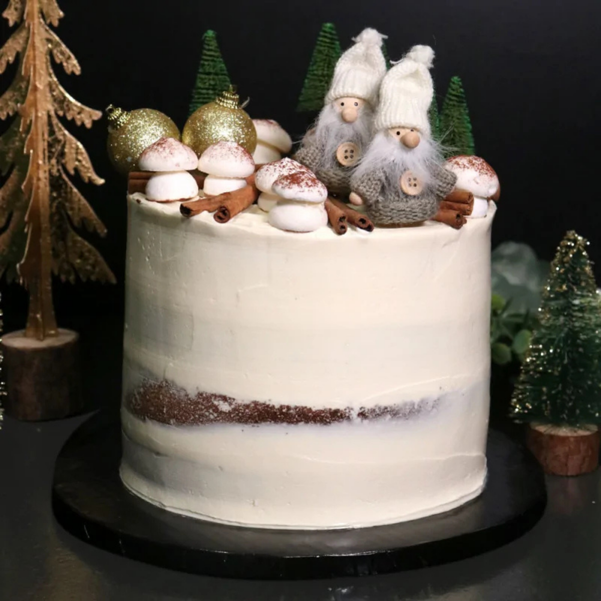Gâteau de Noël décoré de champignons, lutins et sapins, présenté sur un plateau rond noir