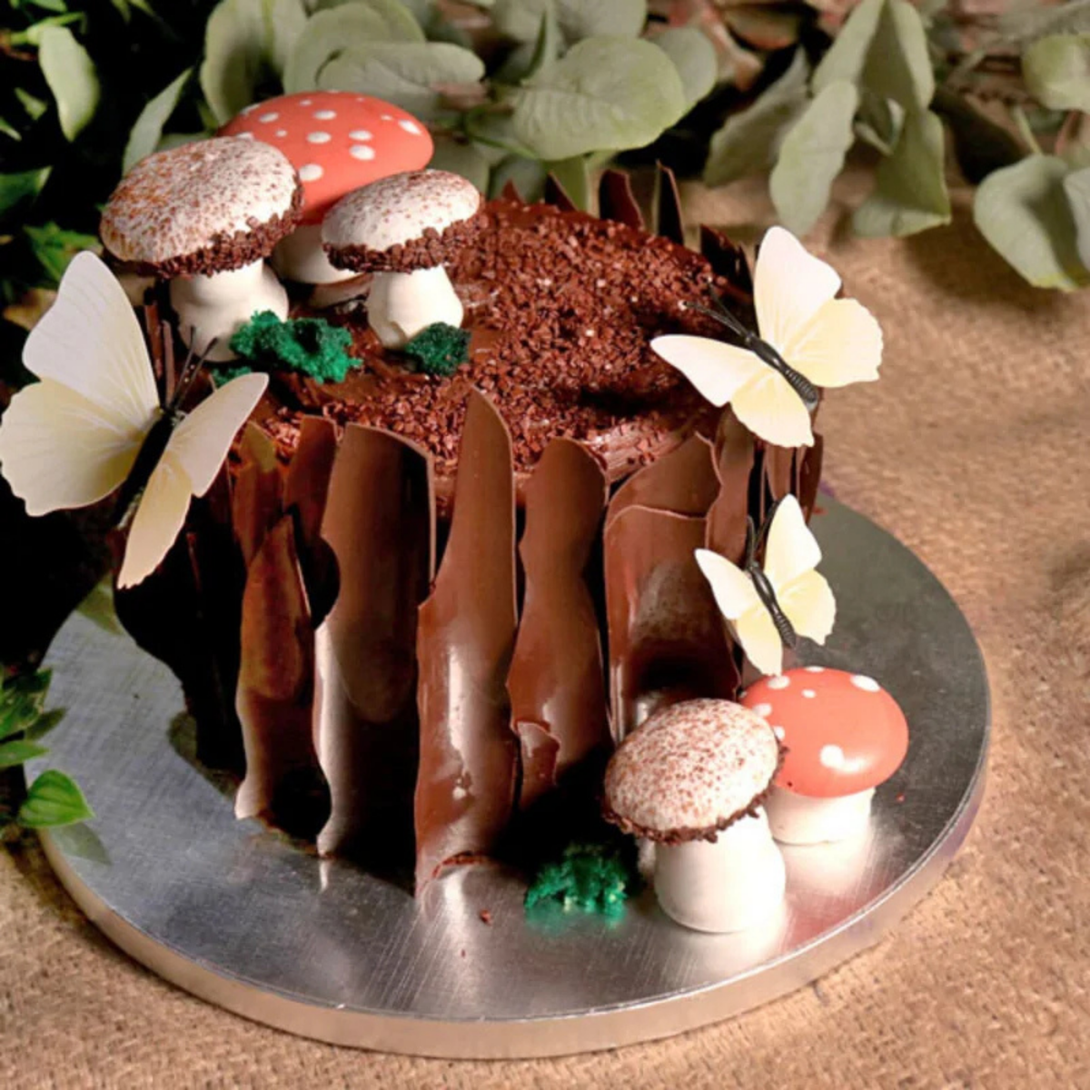 Gâteau au chocolat décoré sur le thème de la forêt avec champignons et papillons, présenté sur un plateau rond argenté