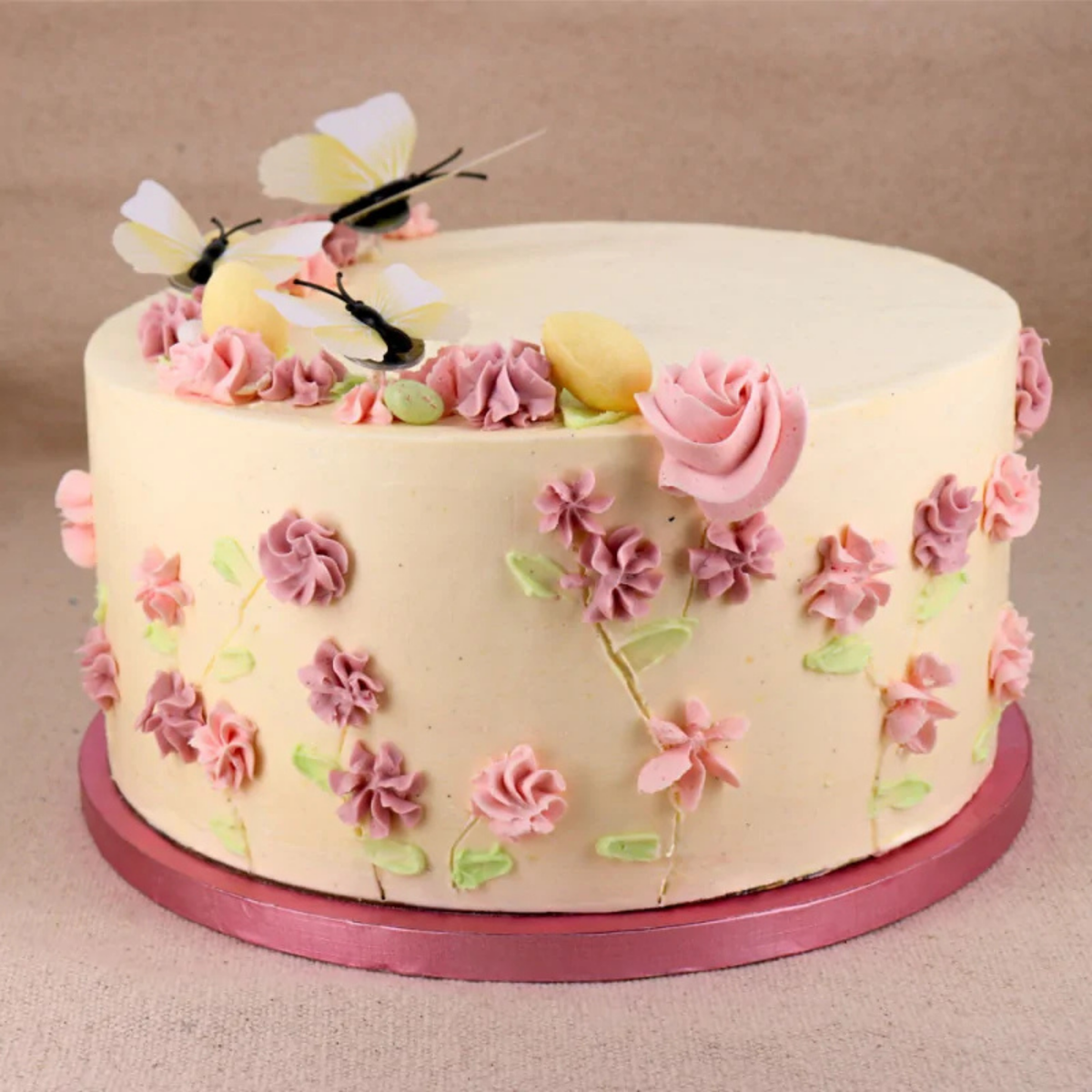 Gâteau fleuri décoré de roses et papillons, présenté sur un plateau rond rose