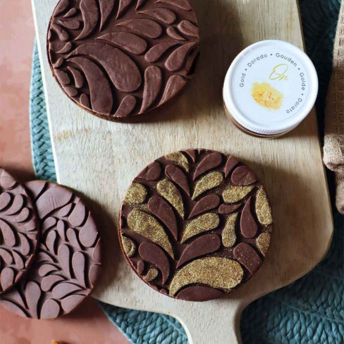 Décorations rondes en chocolat avec motifs végétaux en relief réalisés à l'aide du tapis silicone ScrapCooking Cookina, avec touches dorées.