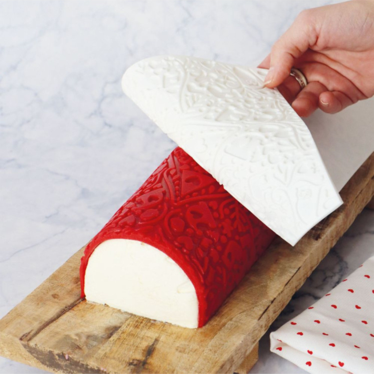 Démoulage du tapis silicone ScrapCooking Cookina blanc sur une bûche de Noël rouge décorée de motifs festifs en relief.