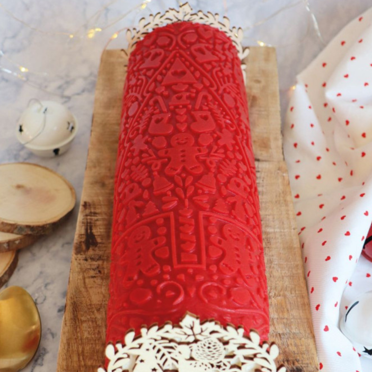 Bûche de Noël rouge avec motifs de sapin, bonhomme en pain d'épices et flocons en relief, réalisée avec le tapis silicone ScrapCooking Cookina.