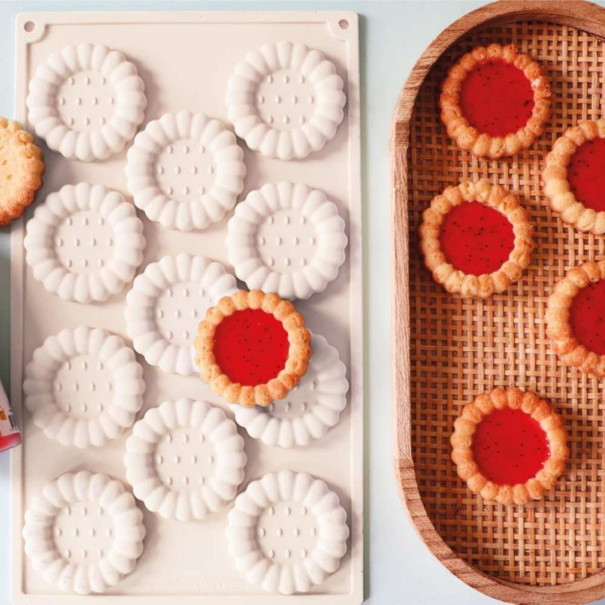 Moule silicone blanc à 12 empreintes rondes cannelées accompagné de tartelettes garnies de confiture rouge.