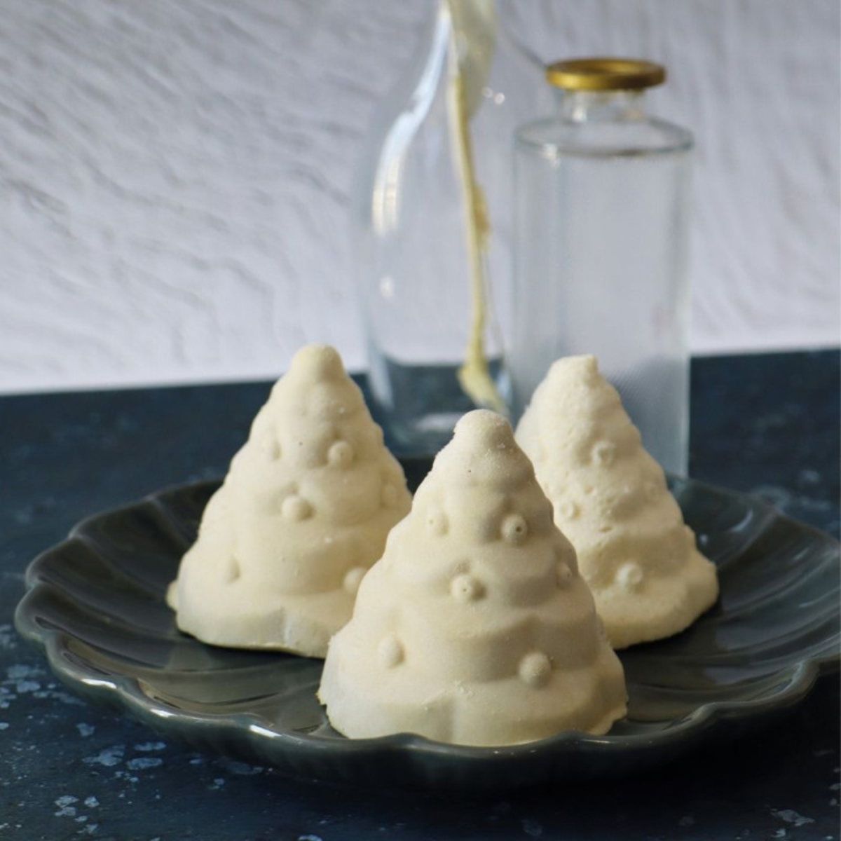 Trois entremets de Noël blancs en forme de sapins 3D, avec guirlandes et boules décoratives en relief.