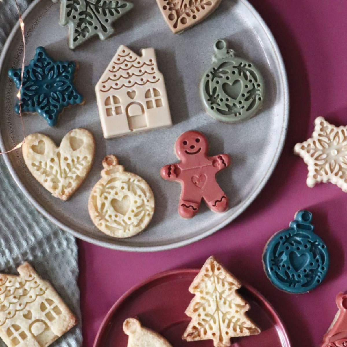 Assortiment de biscuits de Noël décorés en forme de sapins, étoiles, maisons, cœurs et bonhommes en pain d'épices, présentés sur des assiettes.
