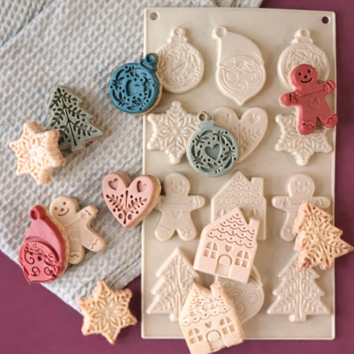 Moule silicone ScrapCooking pour biscuits de Noël accompagné de biscuits colorés aux motifs festifs en relief, sapins, étoiles, maisons et boules de Noël.
