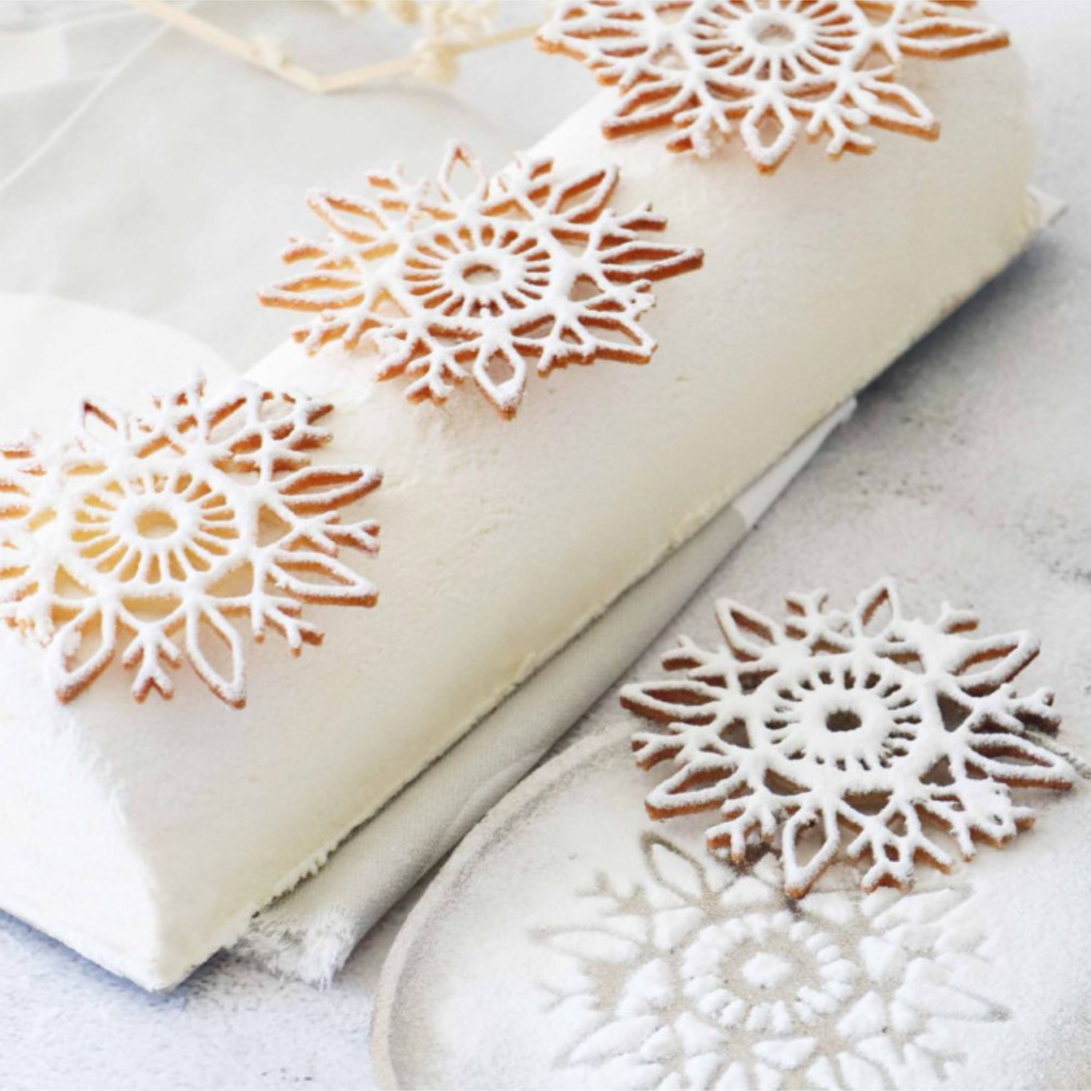 Bûche de Noël blanche décorée de tuiles en forme de flocons de neige dorés et saupoudrés de sucre glace, réalisées avec un tapis en silicone.
